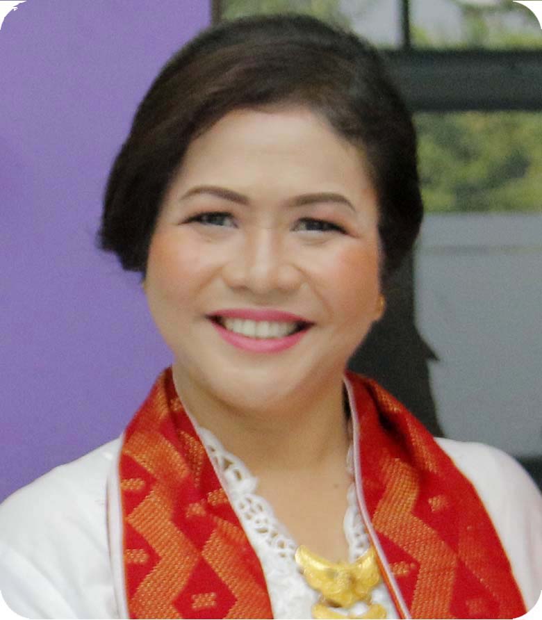 Dr. Karina M. Brahmana - Psikolog profesional wanita berusia 40-an dengan kacamata, mengenakan blazer formal, tersenyum ramah dengan latar belakang ruang kerja akademis